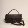 Front view of the Nova Bag in deep brown leather with a structured vanity-box silhouette, a curved top handle, and an adjustable shoulder strap.