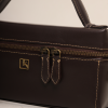 Close-up of the Nova Bag by The Karigar Nepal in chocolate brown leather, showing contrast stitching, antique gold dual zippers, and the signature k logo.