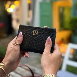 A woman holding a closed Midnight Black croc-embossed genuine leather wallet by The Karigar Nepal featuring a gold k logo.