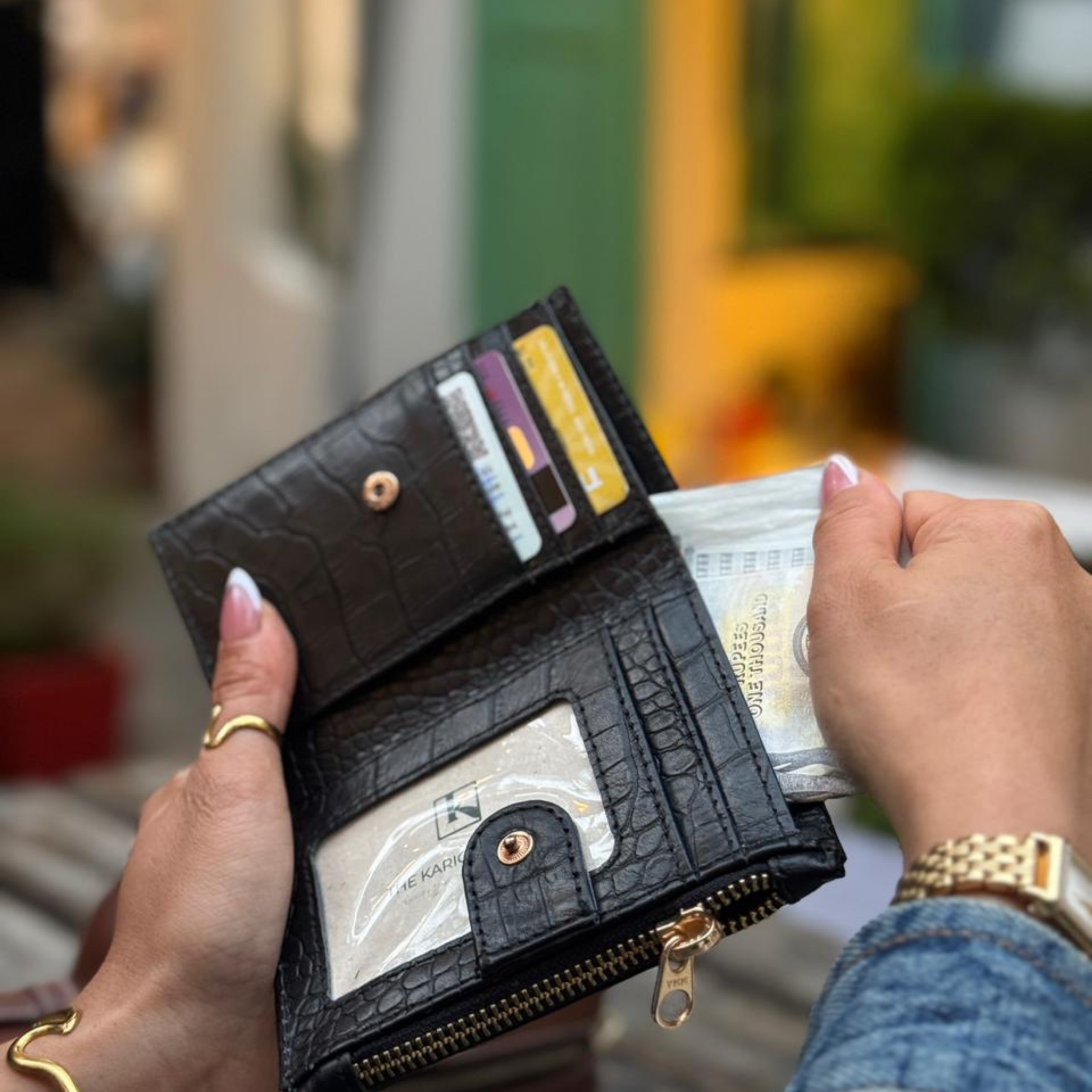 Woman's hands holding an open black leather wallet with currency notes inside, showing the craftsmanship of The Karigar Nepal.